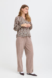 Woman wearing a patterned top and beige pants on a white background